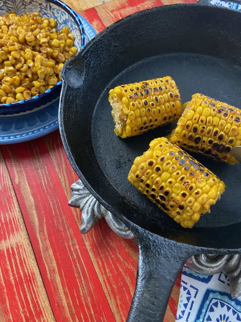 Three roasted corn cobs in a cast iron skilet.