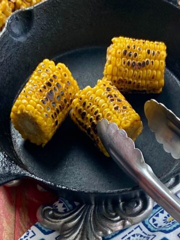 Three roasted corn cobs in a black skillet.