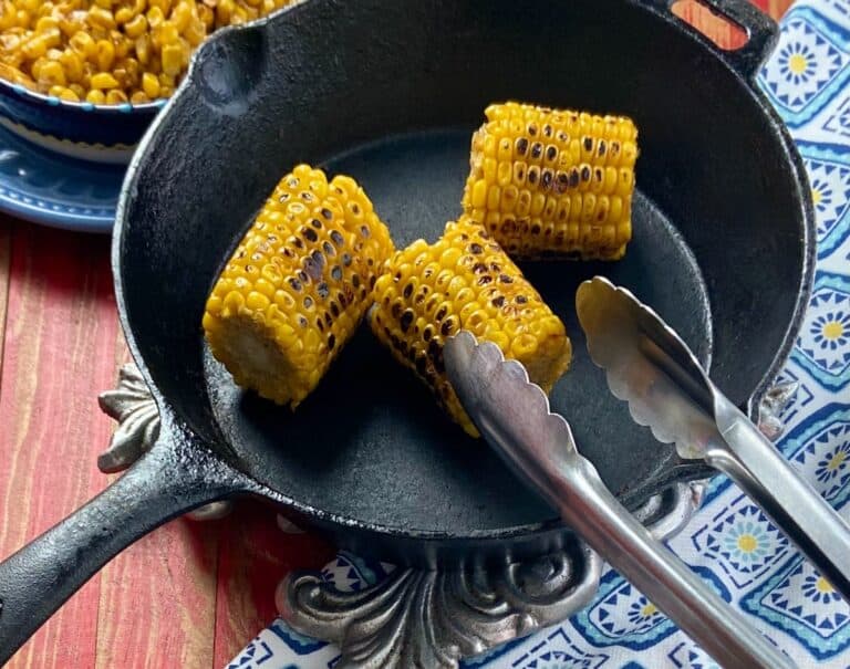 Three roasted corn cobs in a black skillet.