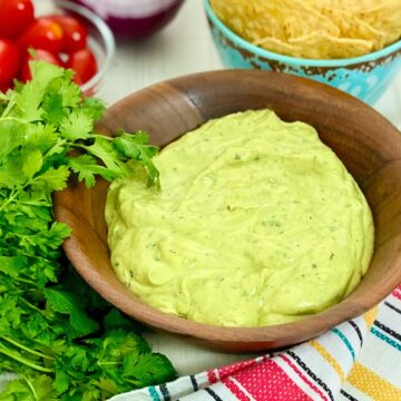 Creamy avocado dip in brown wooden bowl.