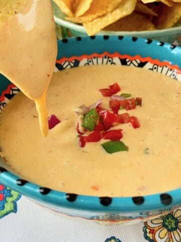 Chile con queso dripping of a yellow tortilla chip over a bowl of queso.