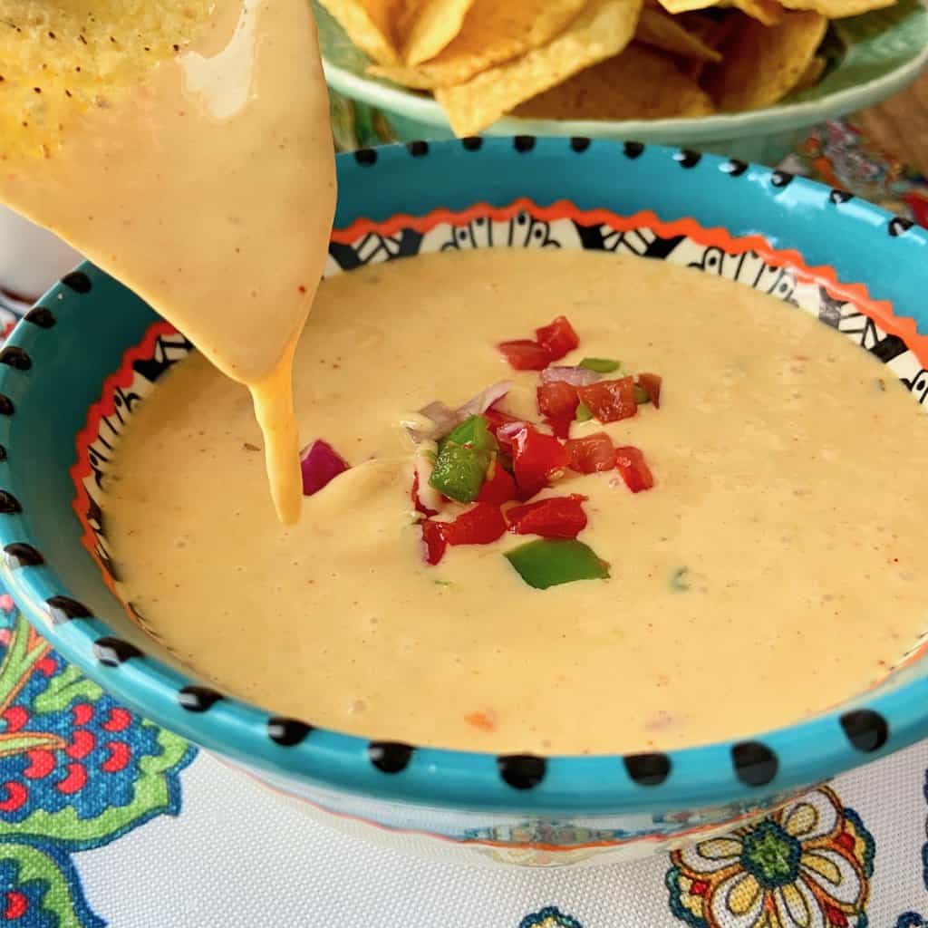 Chile con queso dripping of a yellow tortilla chip over a bowl of queso.