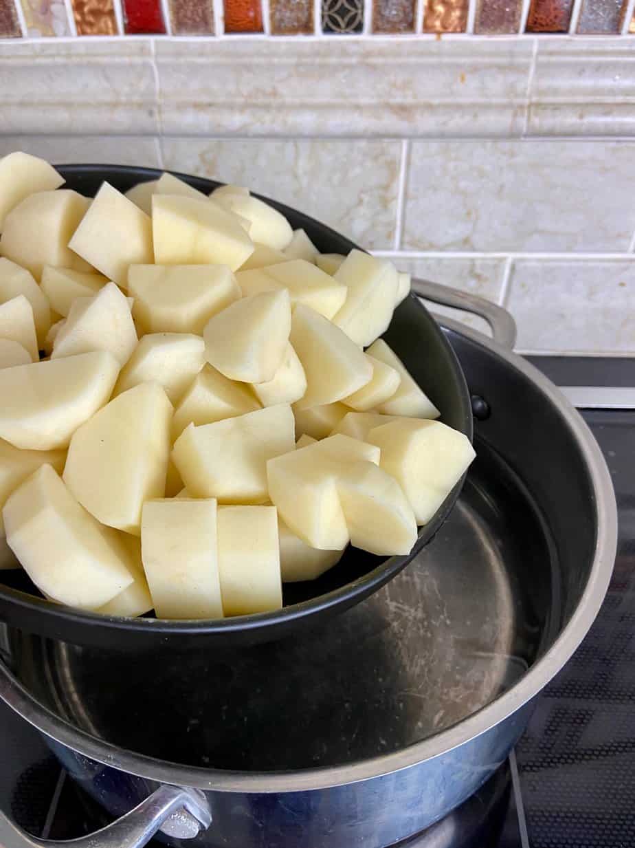 Cubed russet potatoes going into stockpot of water.