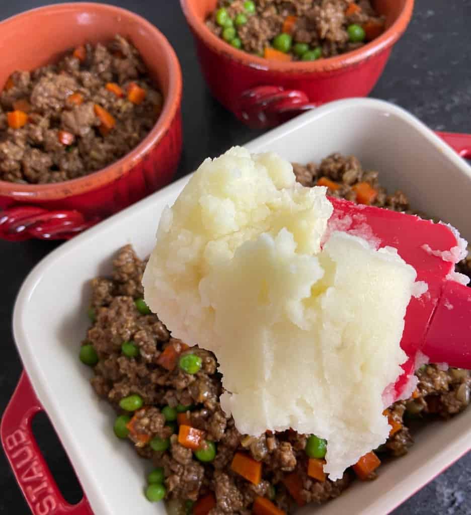 Mashed potatoes being spread over meat filling with spatula.