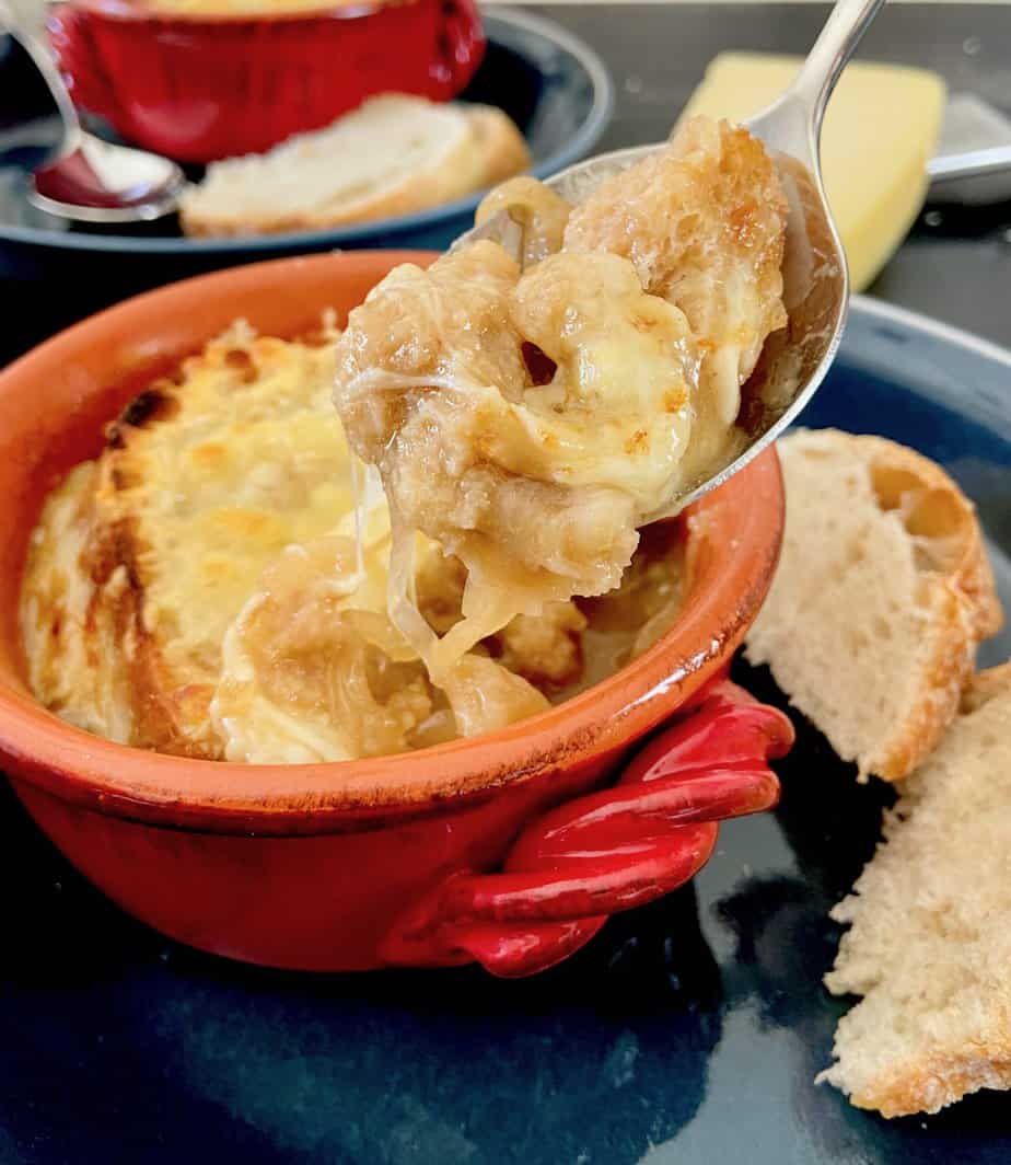 French onion soup on spoon over red bowl.