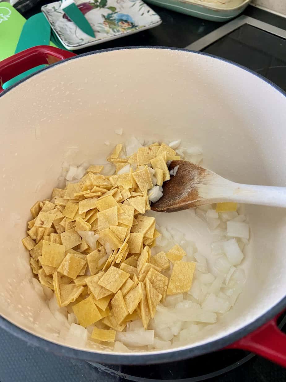 White onions and torn corn tortillas in stockpot with oil.