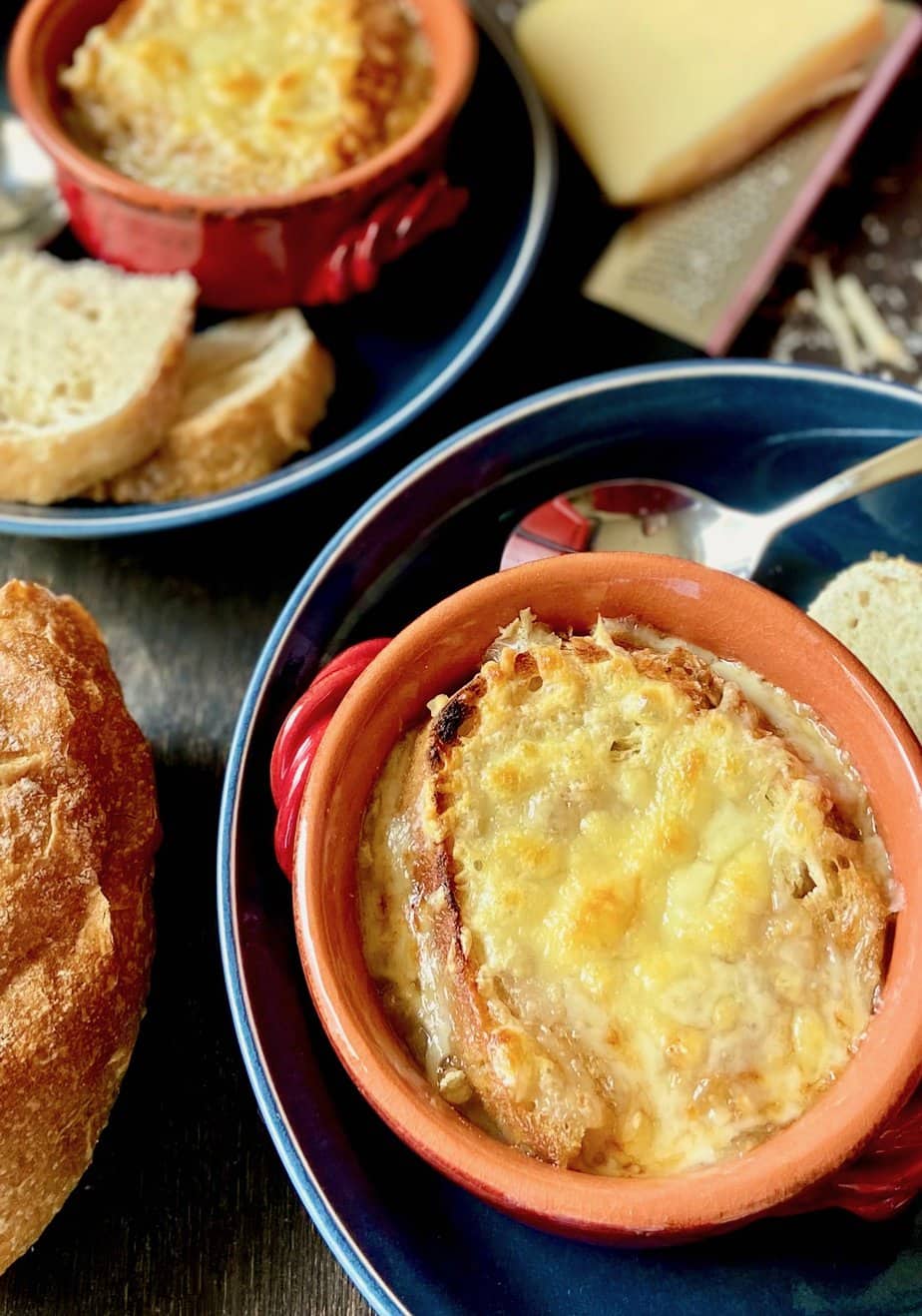 French onion soup in a red bowl next to a loaf of bread.