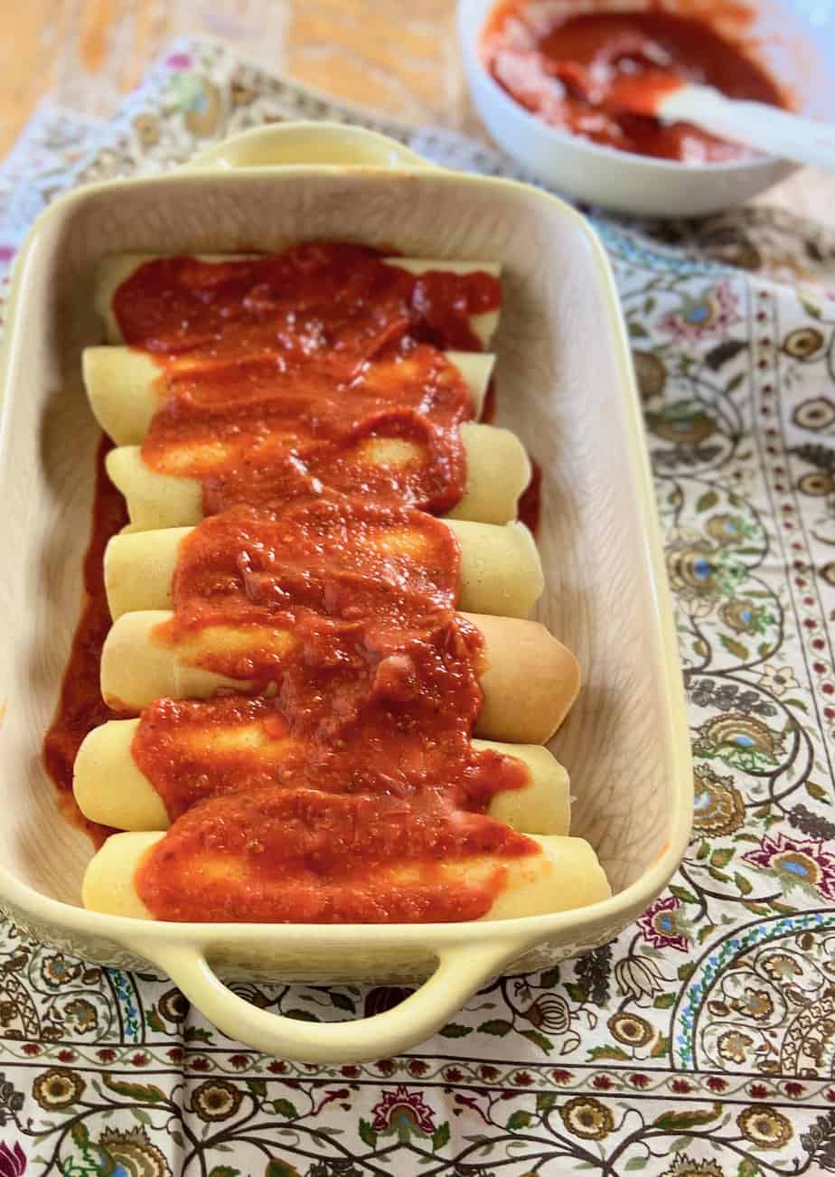 Manicotti in baking dish topped with red pasta sauce.