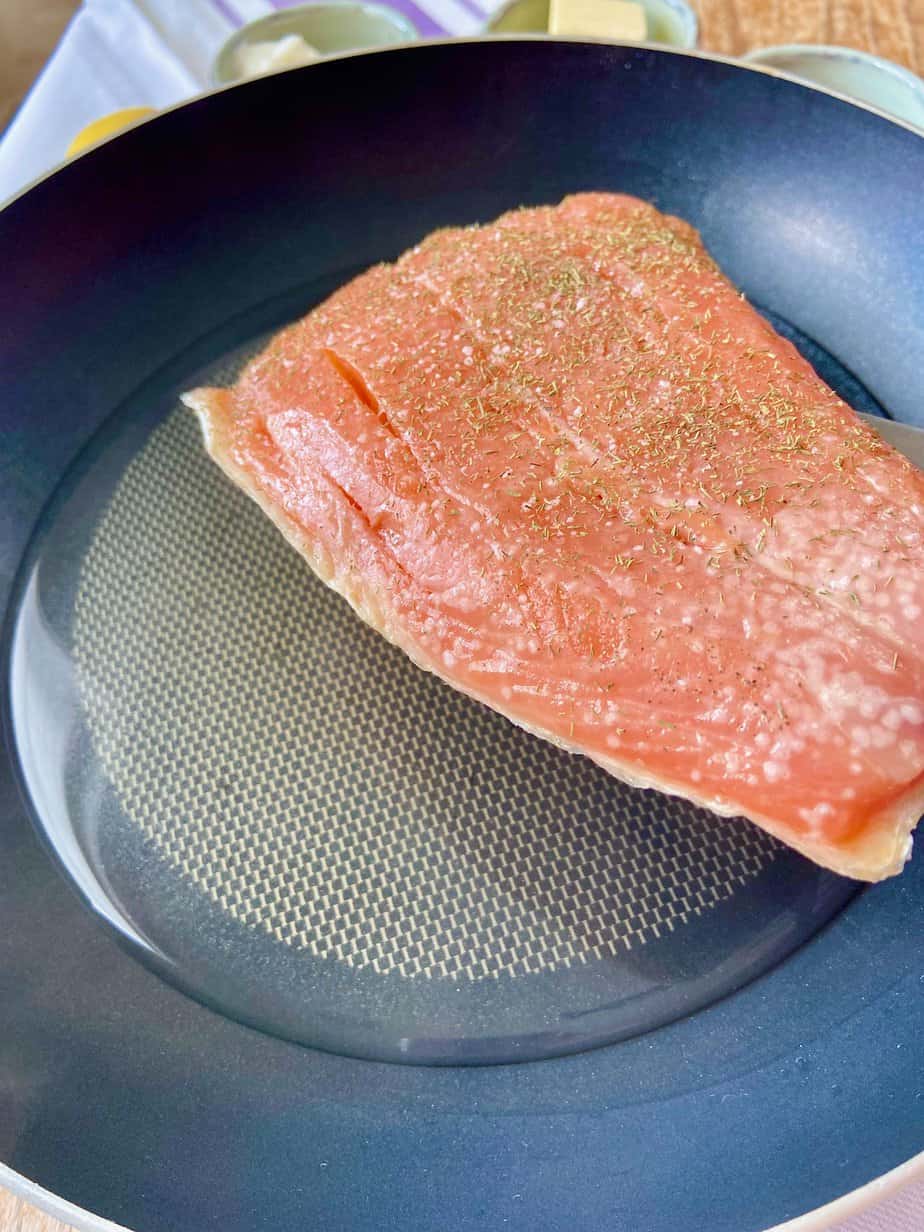 Fresh salmon fillet in skillet with a little water.