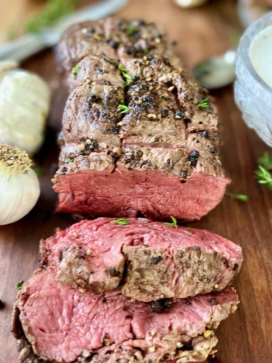 Sliced beef tenderloin on wooden platter.