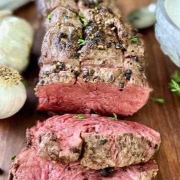 Sliced beef tenderloin on wooden carving platter.