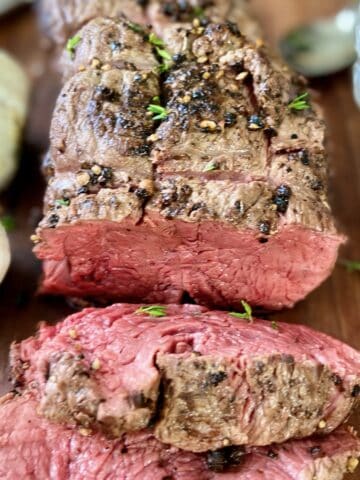 Sliced beef tenderloin on wooden carving platter.