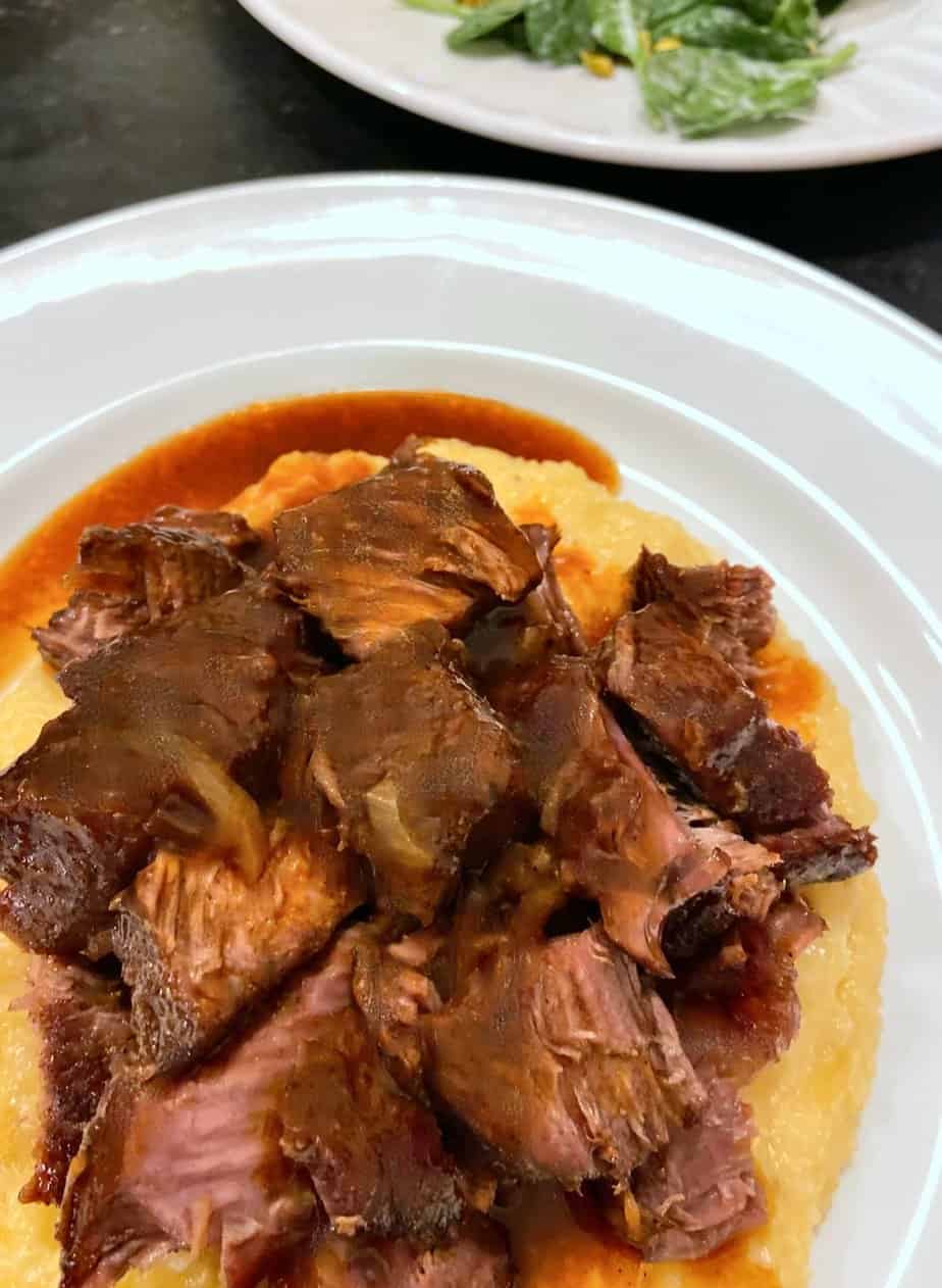 Braised short ribs and cheese grits on white plate.