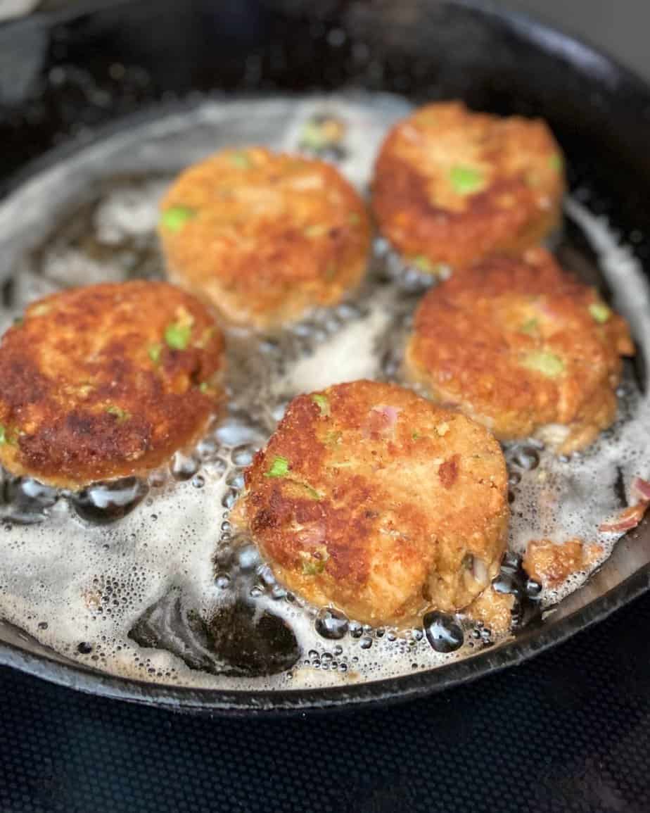 Salmon patties cooking in cast iron skillet.