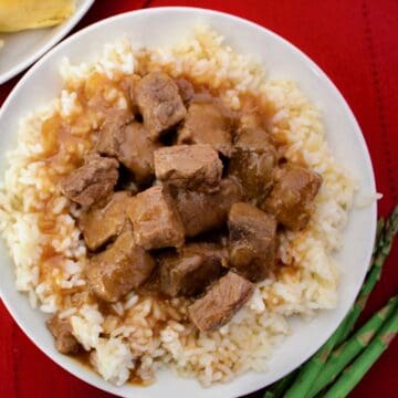 Beef tips with rice and brown gravy in white bowl.