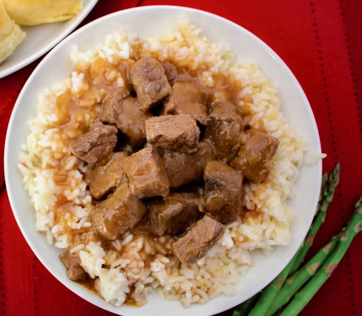 Beef tips with rice and brown gravy in white bowl.