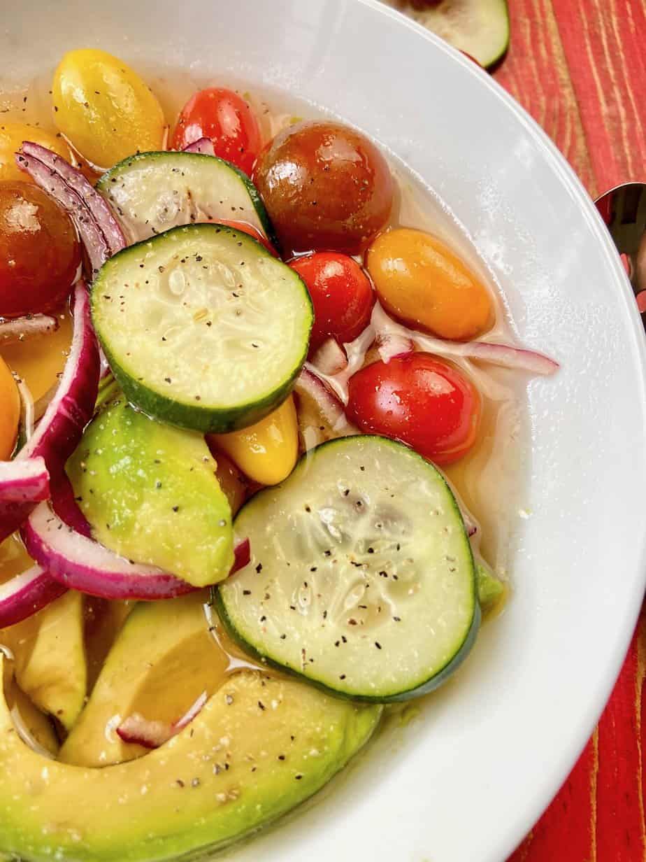 Marinated cucumber tomato onion and avocado salad in white bowl.
