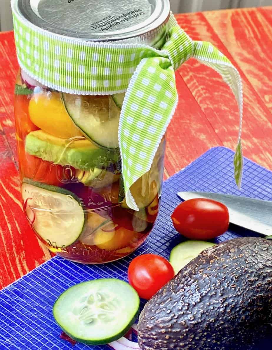 Marinated cucumber tomato salad in mason jar with decorative bow.