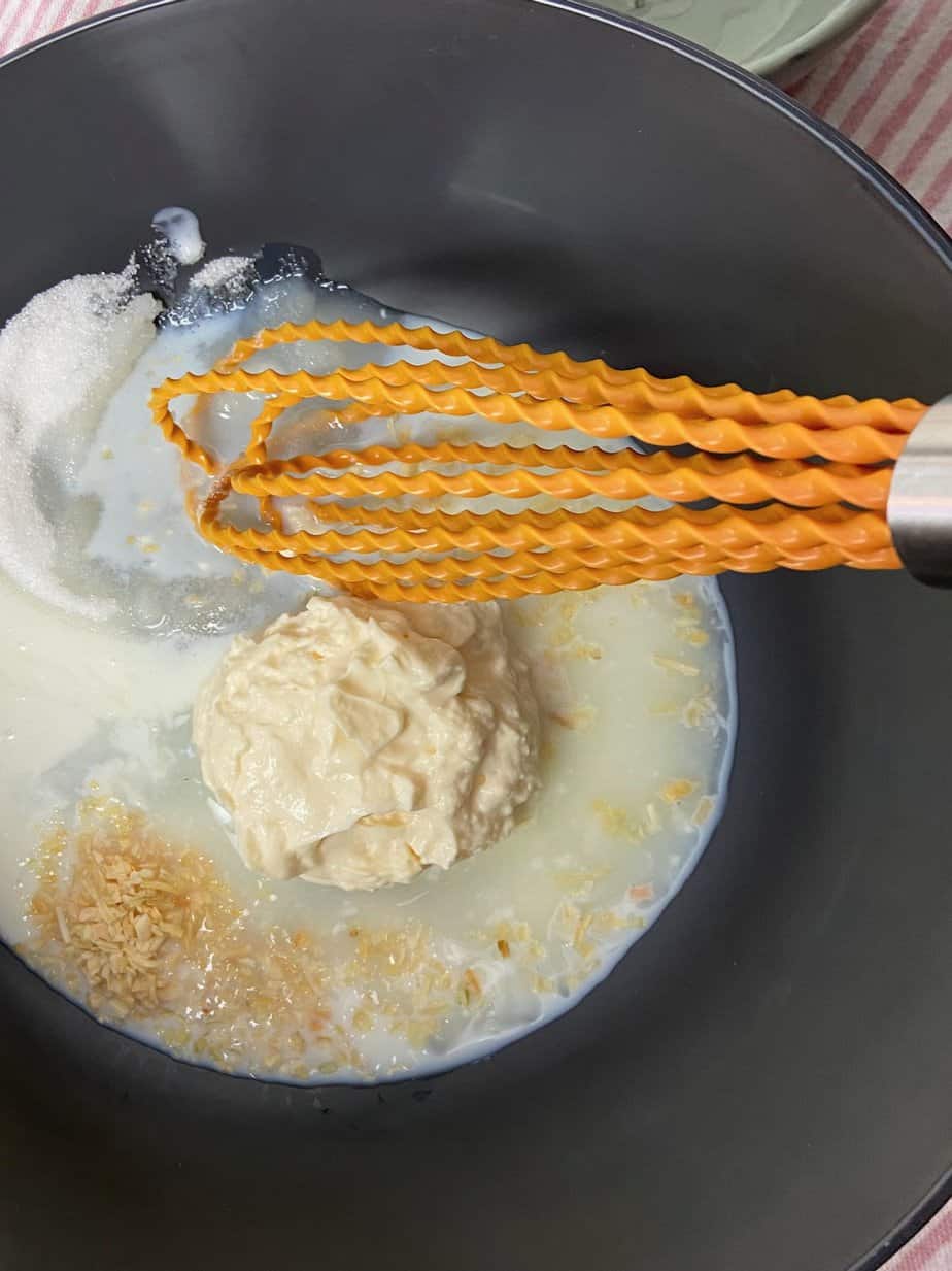 Coleslaw dressing ingredients in black bowl with orange whisk.