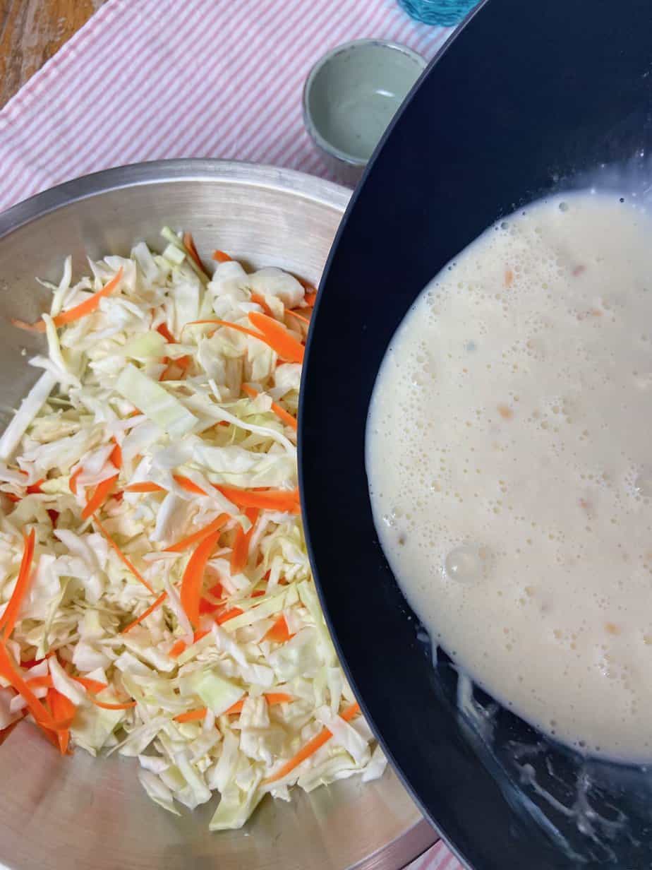 Coleslaw dressing being poured over shredded cabbage and carrots.