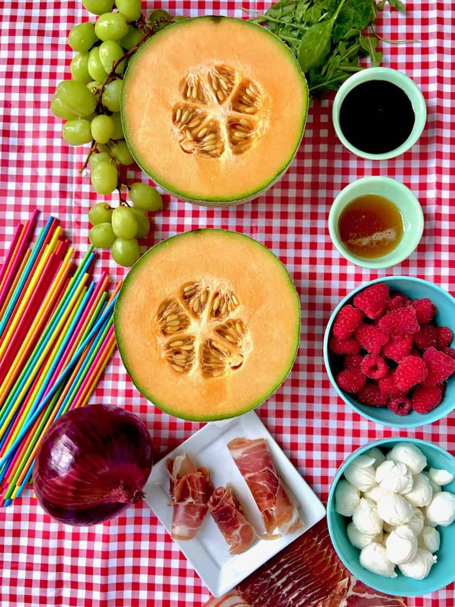 Fruit kabob ingredients on red checkered tablecloth.