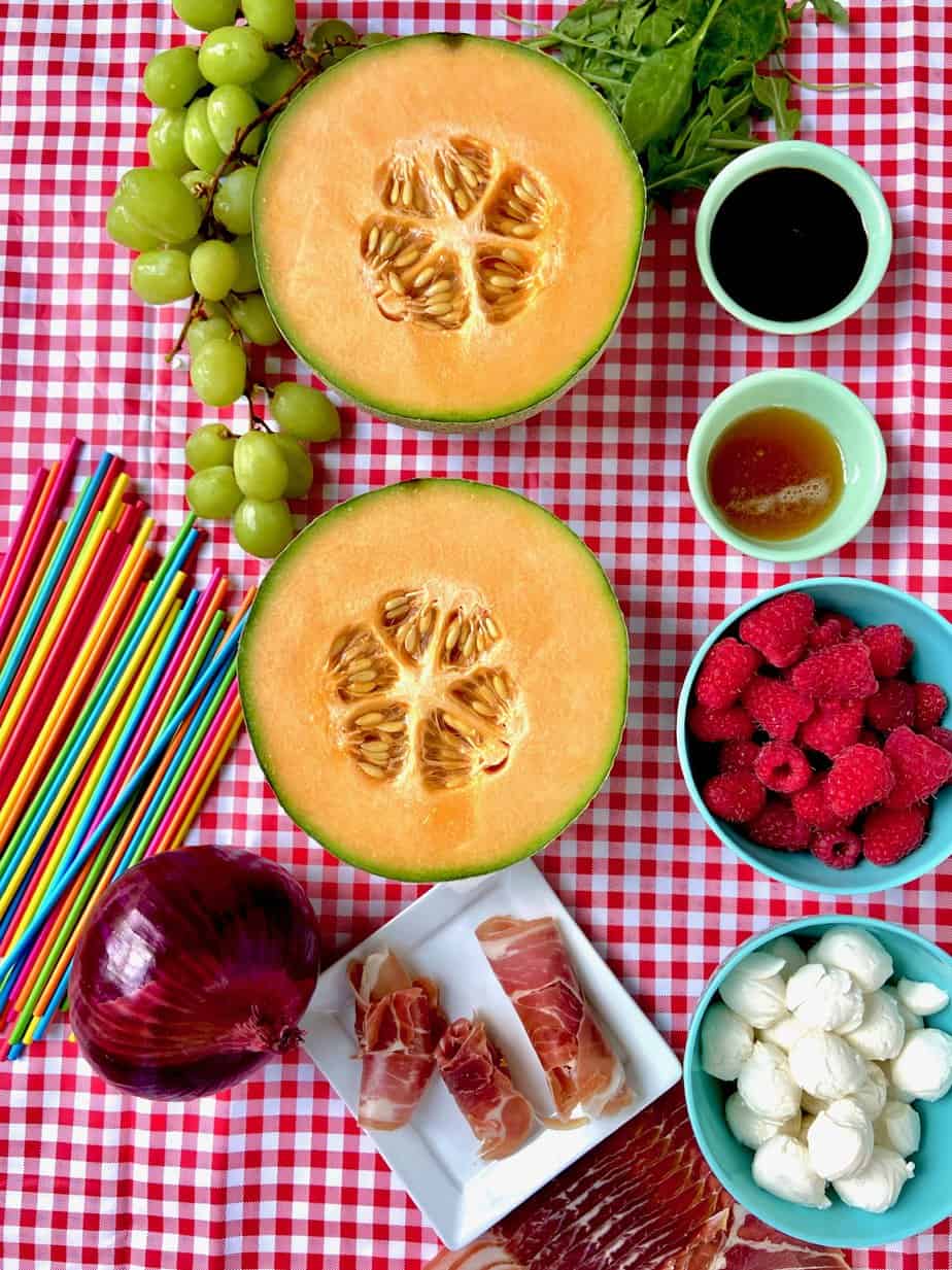 Fruit kabob ingredients on red checkered tablecloth.