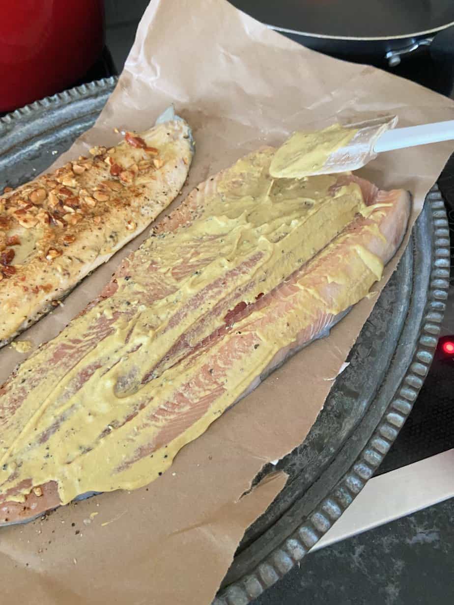 Trout fillet being coated with Dijon mustard on spatula.