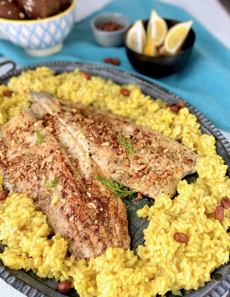 Two almond crusted rainbow trout fillets on serving platter with yellow rice.