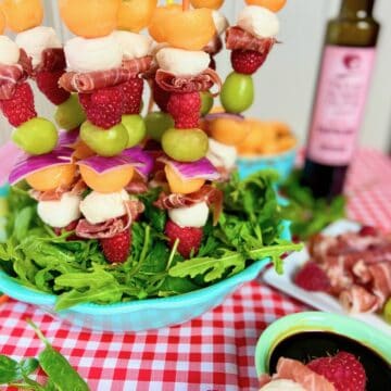 Fruit kabobs with cantaloup and prosciutto in blue bowl.