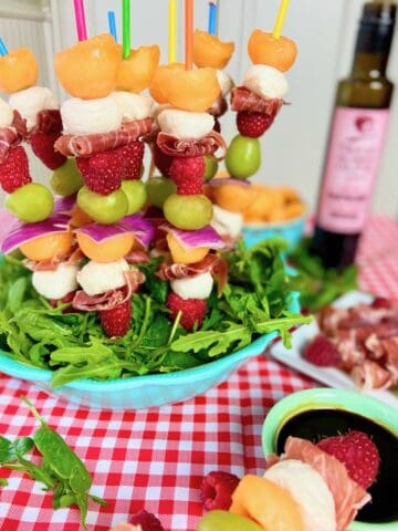 Fruit kabobs with cantaloup and prosciutto in blue bowl.