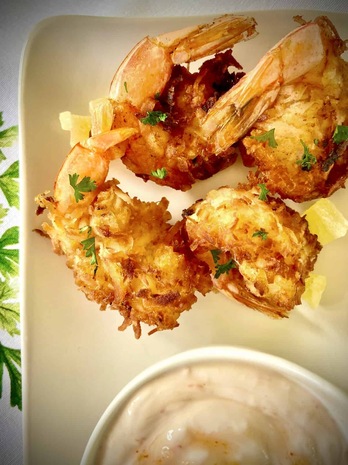 Fried coconut shrimp on platter next to dipping sauce.