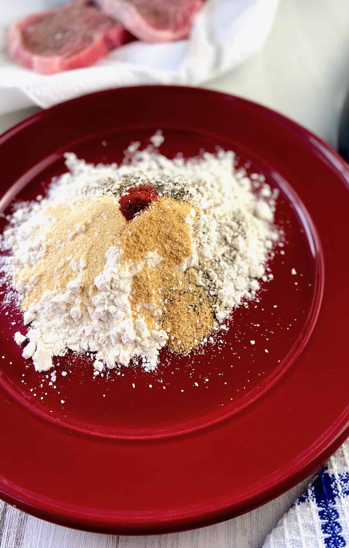 Dry ingredients for pan fried pork chops on red plate.