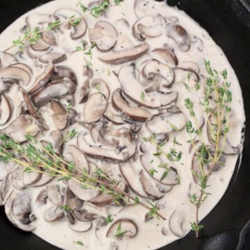 Creamy mushroom sauce in saucepan with fresh thyme sprigs.