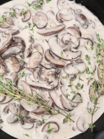 Creamy mushroom sauce in saucepan with fresh thyme sprigs.