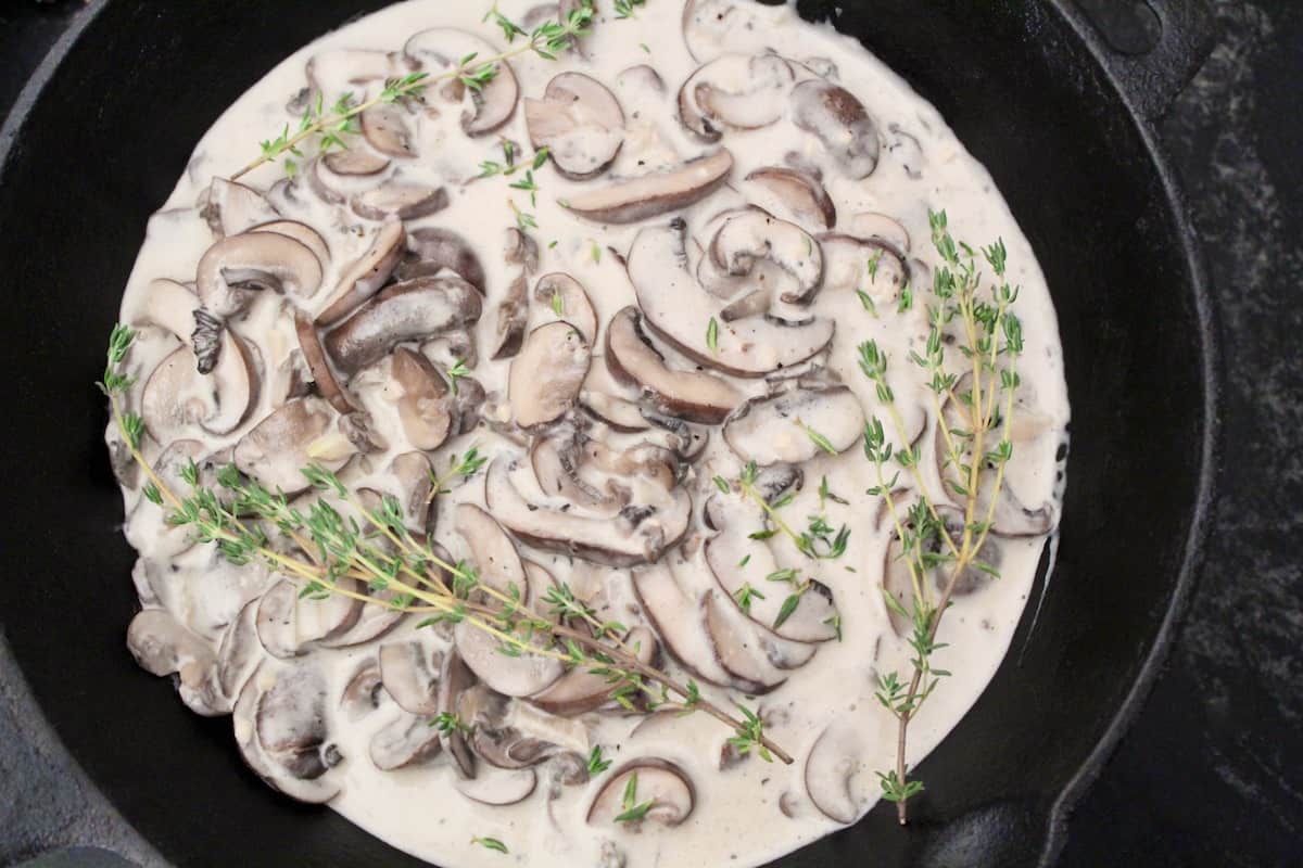 Creamy mushroom sauce in saucepan with fresh thyme sprigs.