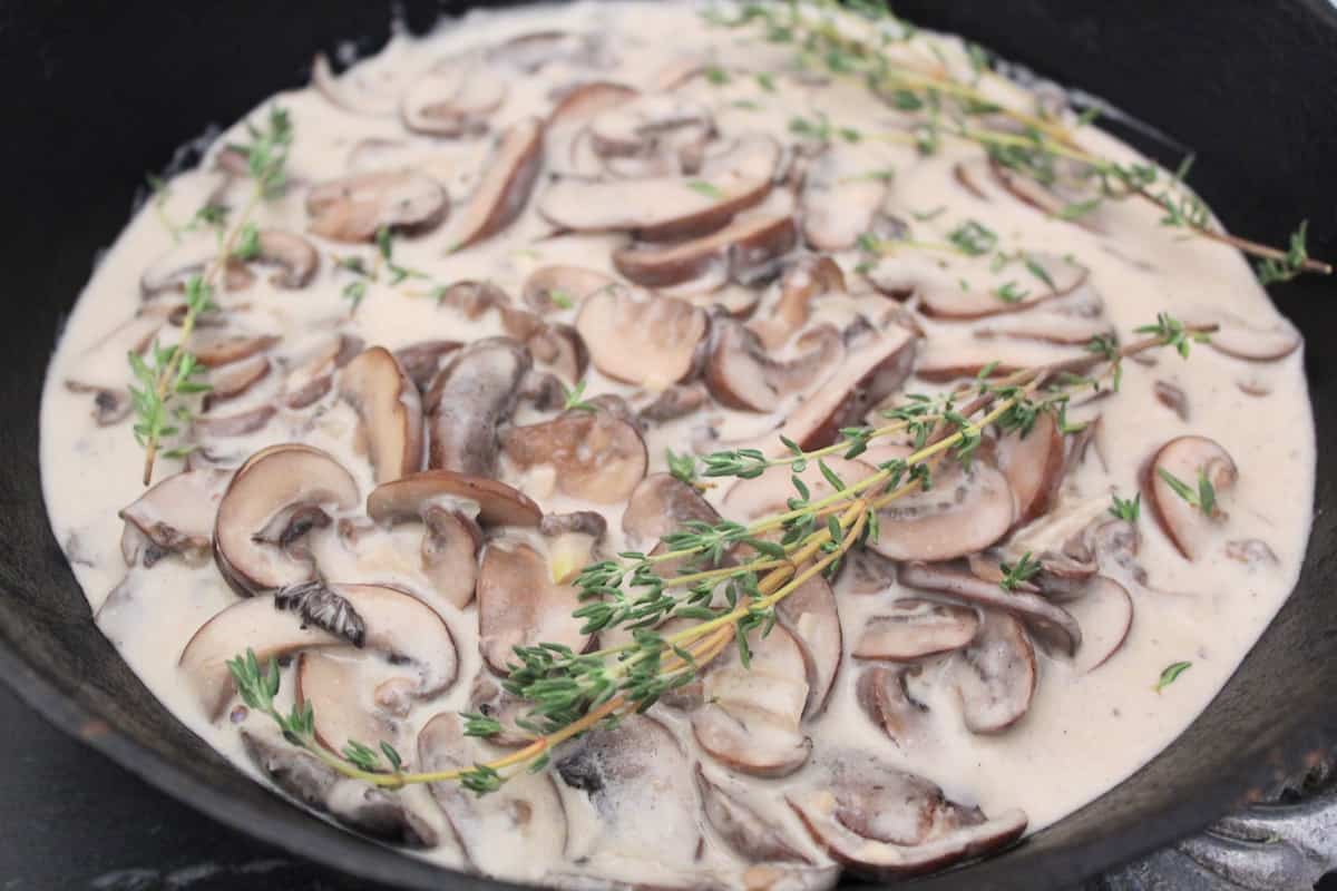 Mushroom cream sauce in saucepan with fresh thyme sprigs.