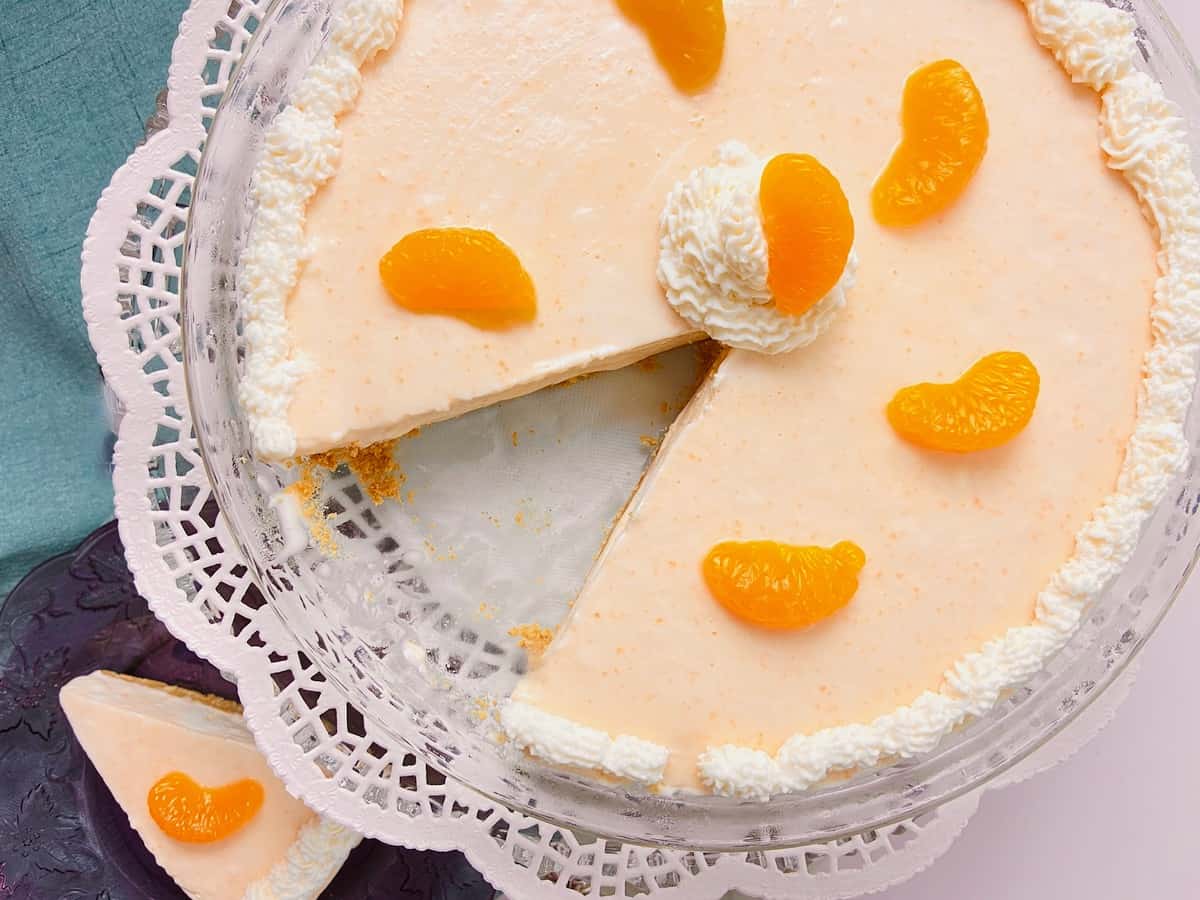 Orange Creamsicle icebox pie on glass pedastal with white doily underneath.