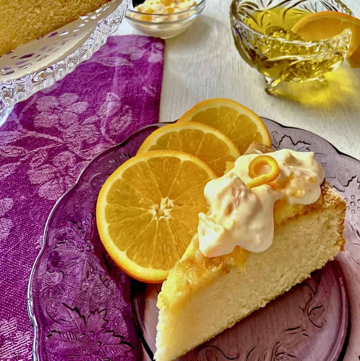 Slice of orange olive oil cake with creme fraiche on purple plate.