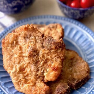 Crispy golden pan fried pork chops on blue plate.