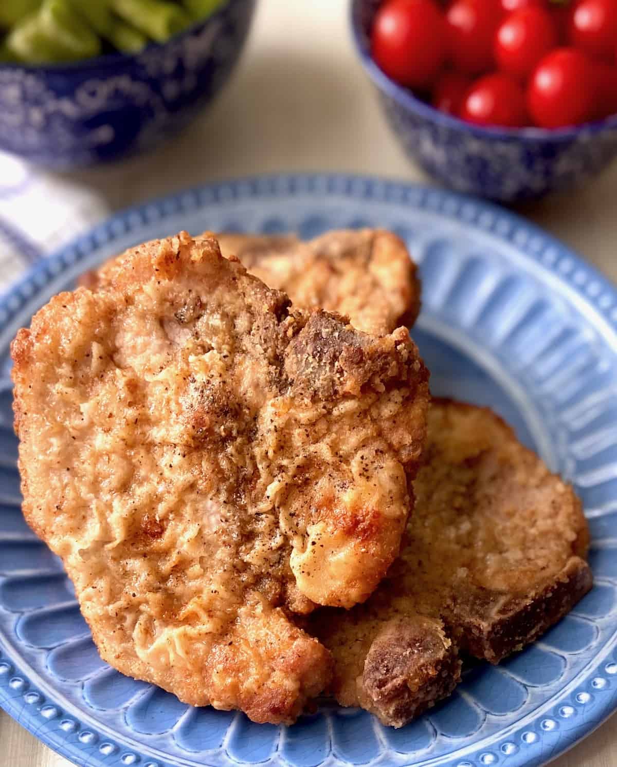 Crispy golden pan fried pork chops on blue plate.
