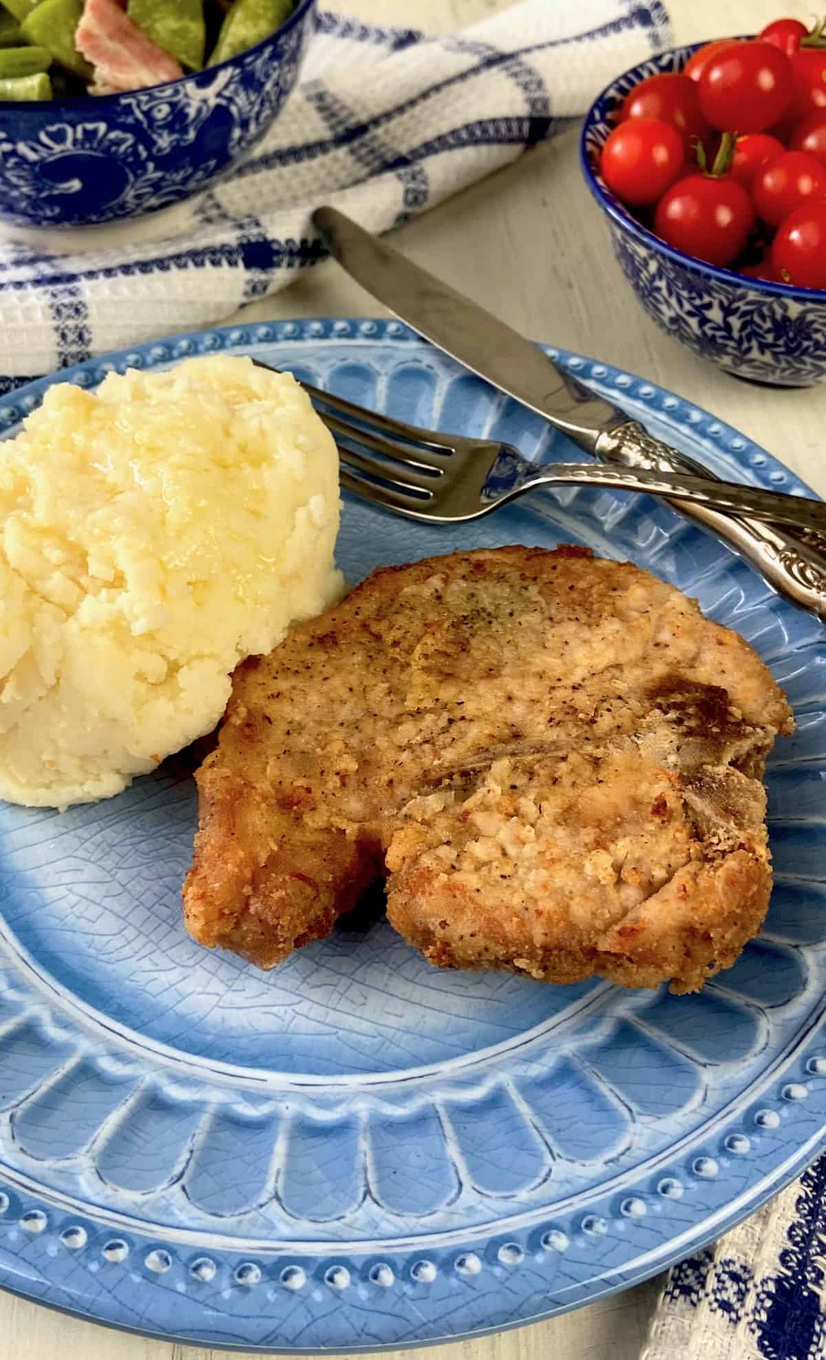 Pan fried pork chop and mashed potatoes on blue plate.