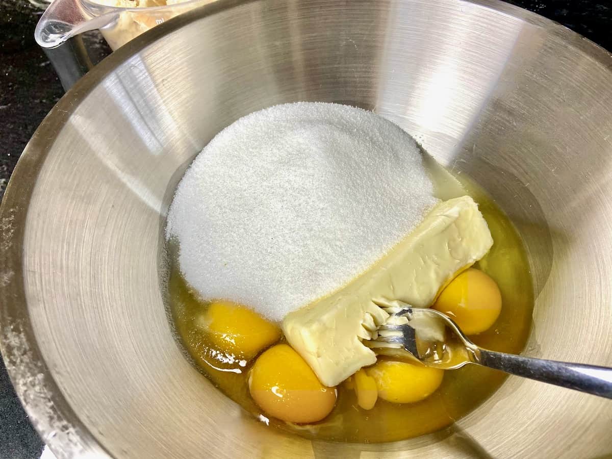 Eggs, sugar and butter in metal mixing bowl with a fork.