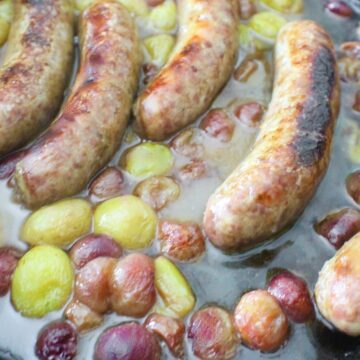 Italian sausage links and grapes in cast iron skillet.
