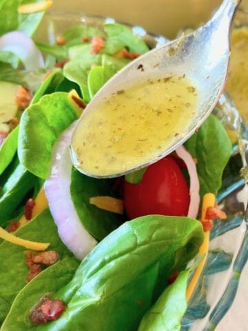 Low sodium salad dressing in spoon drizzling over salad.