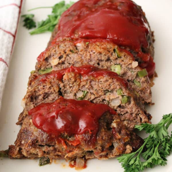 Sliced meatloaf with tomato sauce on white plate.