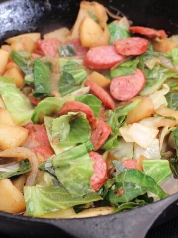 Cabbage, sausage and potatoes in cast iron skillet.