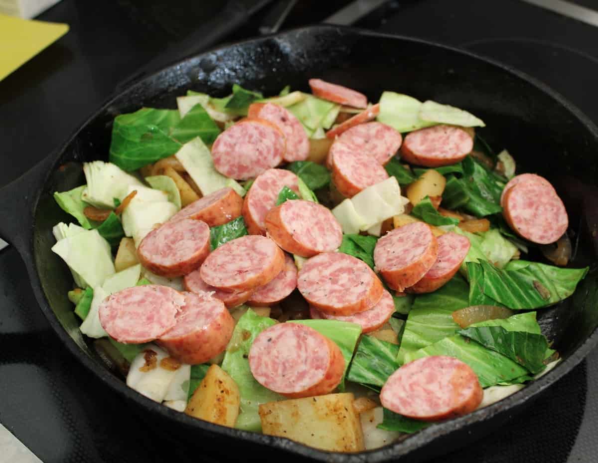 Cabbage, sausage and potatoes in cast iron skillet.