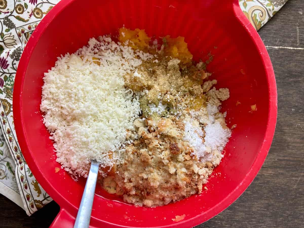 Cheee, eggs and seasonings in squash mixture in red bowl.