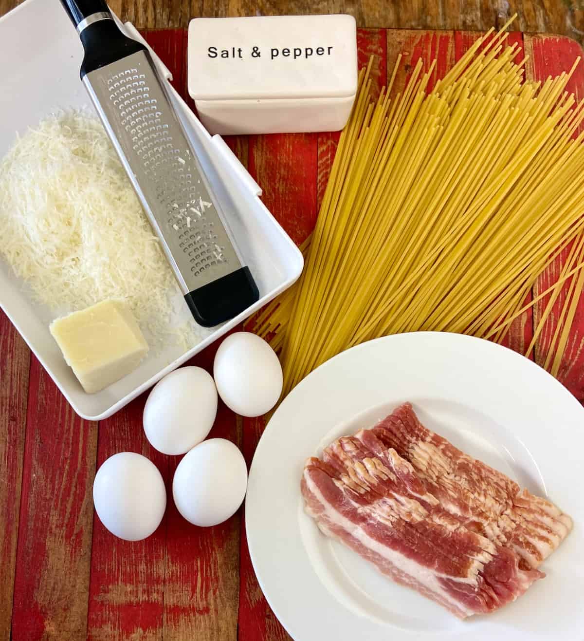 Ingredients for pasta carbonara on red wooden table.