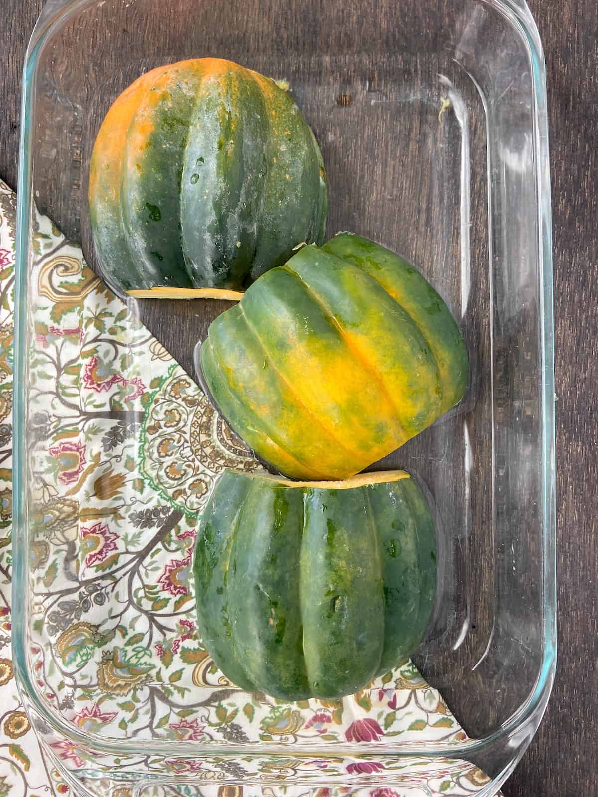 Three halves of acorn squash in pyrex bowl cut side down.